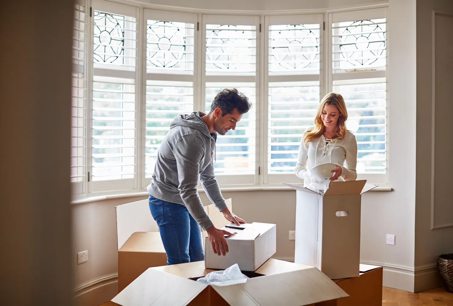 A couple unpacking moving boxes in the bay window of their new home